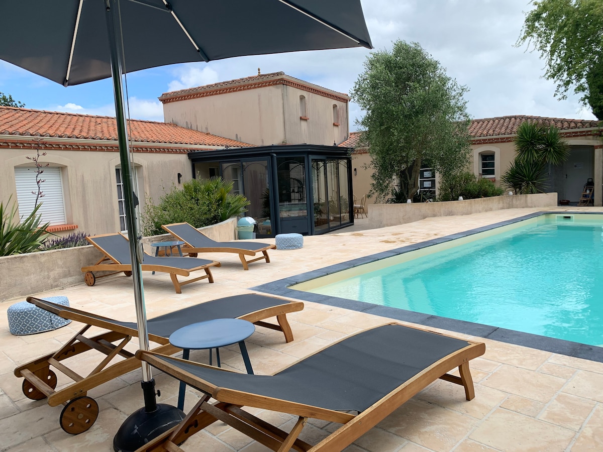 A well-maintained outdoor pool area is highlighted, featuring a turquoise swimming pool surrounded by a sun terrace. Comfortable lounge chairs are present along with an umbrella for shade. Nearby, a glass structure offers a view of the lush landscaping that enhances the tranquil setting.