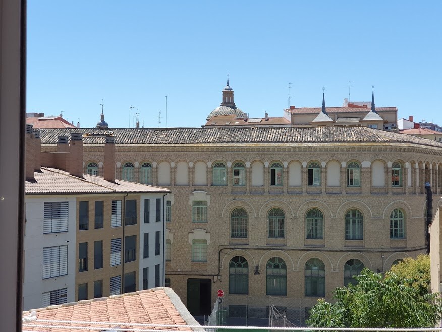 A view of the surrounding area features a historic building with arched windows and a decorative dome. The scene includes additional residential structures, showcasing diverse architectural styles under a clear blue sky.
