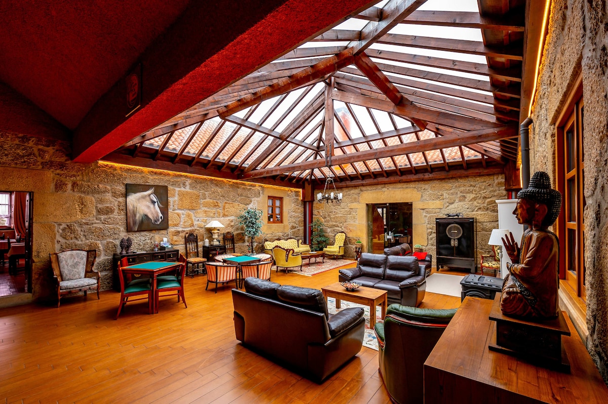 An open and airy living area is highlighted by a wooden ceiling with a skylight, allowing natural light to fill the space. Comfortable seating is arranged around a coffee table, and decorative elements, including a statue and textured walls, provide visual interest.