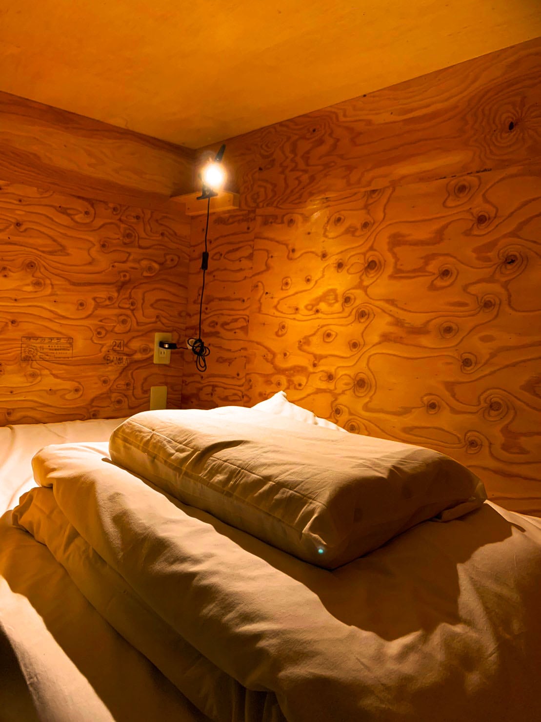 A cozy sleeping area is displayed, featuring a spacious bed with stacked pillows. Soft bedding is complemented by warm wooden walls, which create a calming environment. A light fixture is mounted above the bed, providing illumination for nighttime reading or relaxation.