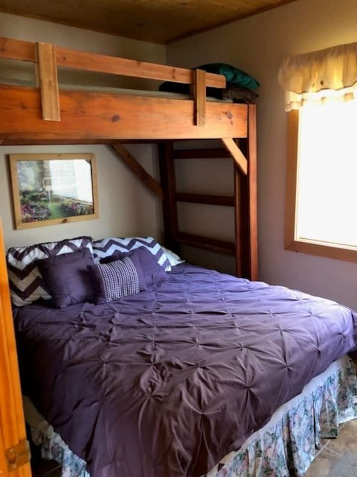 Cama de matrimonio con litera individual encima.  Banco para maleta, estante de armario abierto con perchas.  Este dormitorio tiene vistas al lago.