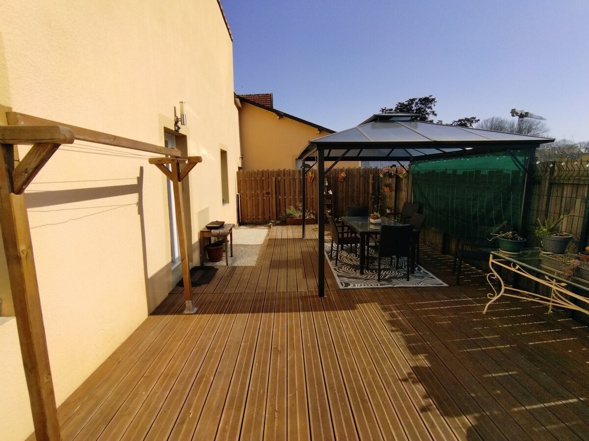 A private terrace features a wooden deck complemented by a pergola. Seating arrangements under the pergola provide shaded areas for relaxation. The surrounding greenery and fencing enhance the outdoor space's tranquility, with ample sunlight streaming down, creating a welcoming atmosphere for outdoor enjoyment.