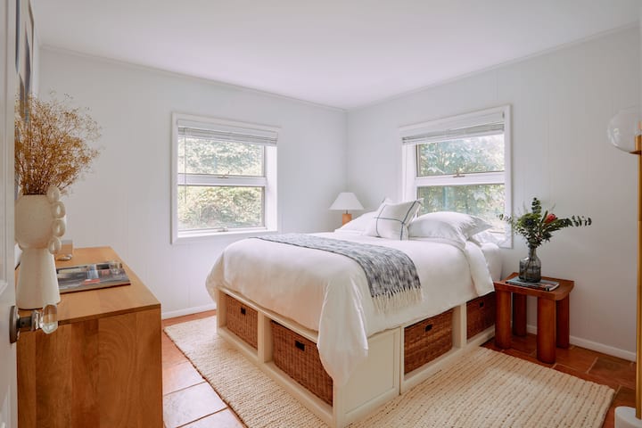 Dormitorio # 3: dormitorio moderno y elegante con una lujosa cama tamaño queen con almacenamiento incorporado, detalles decorativos naturales y grandes ventanales con vistas a la vegetación. Perfecto para noches de descanso en un entorno sereno y elegante, que ofrece comodidad y practicidad.