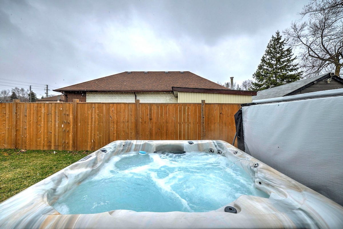 An outdoor hot tub is filled with bubbling water, surrounded by a wooden fence that offers privacy. The cloudy sky above adds a serene atmosphere to the space, highlighting the hot tub as a year-round relaxation option.