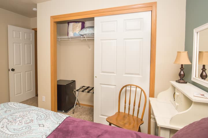 Private room with queen bed, small desk, large closet, refrigerator, luggage rack, iron, and ironing board  