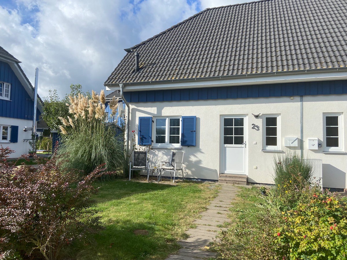The exterior features a two-story house with a welcoming entrance and blue shutters. A stone pathway leads to the front door, bordered by neatly manicured grass and flower beds. Nearby, ornamental grasses and shrubs add a natural touch to the inviting atmosphere.