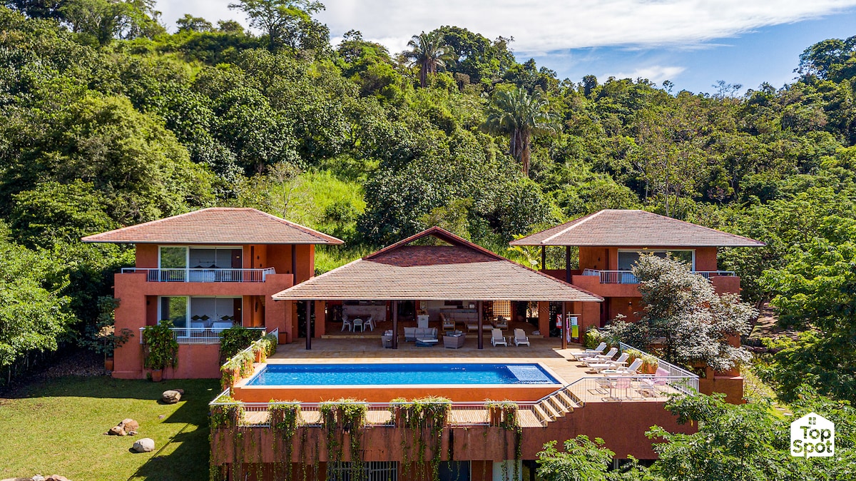 A spacious two-story house is visually connected to the surrounding landscape, featuring a well-maintained private pool. The structure is complemented by ample outdoor seating and lush tropical gardens, providing a serene environment for relaxation.