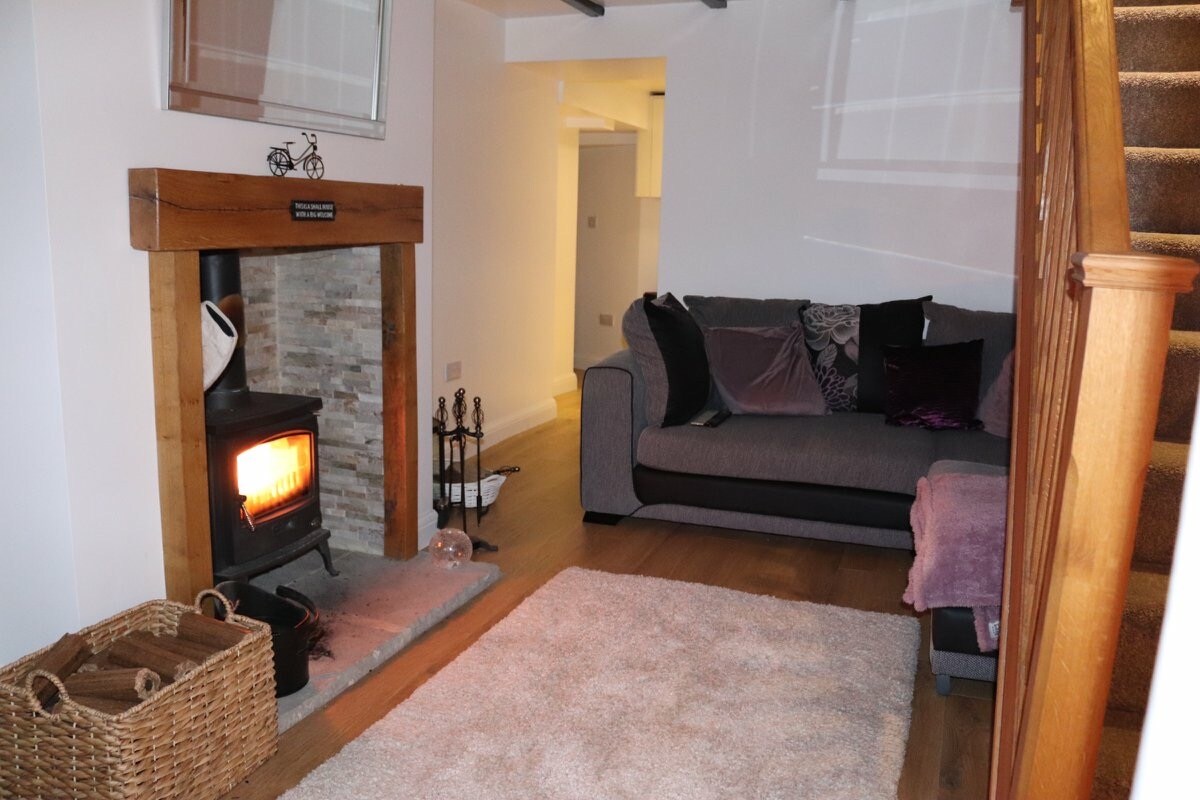 A cozy living area is highlighted by a modern fireplace with a decorative stone surround. A plush sofa is positioned nearby, complemented by soft cushions. A textured area rug covers the wooden floor, adding warmth to the space. Natural light is filtered through the windows.