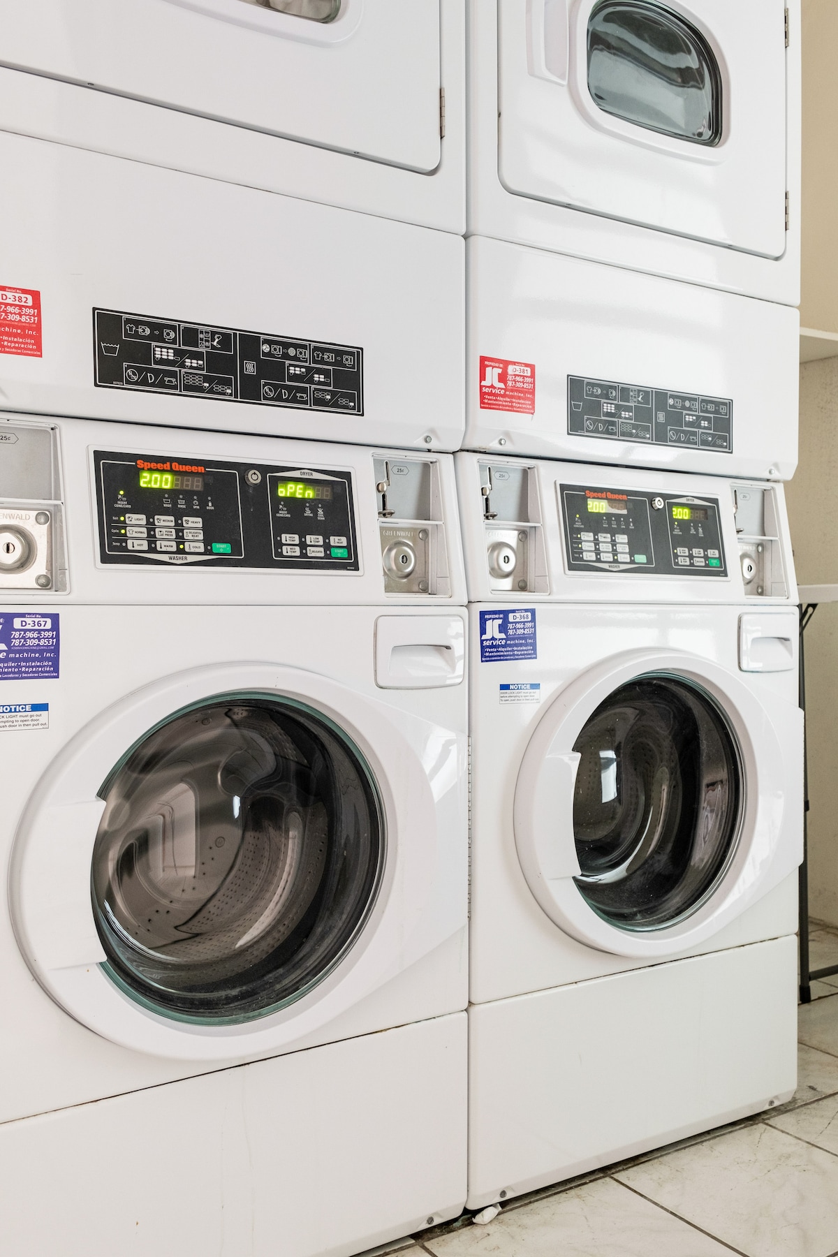 A stacked washer and dryer unit is presented in a clean, modern laundry corner. Control panels with clear displays are positioned on the front, indicating settings for each appliance. White cabinetry is visible above the machines, contributing to an organized space.