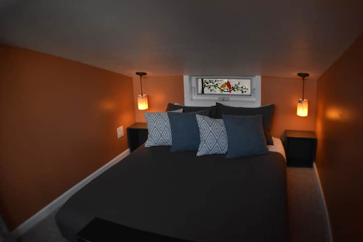 The master loft has a generous Queen-sized mattress with access on both sides, granite pendant lights, 2 small nights stands, a unique bird-themed stained glass art window, and a USB plug for your device-using convenience.
