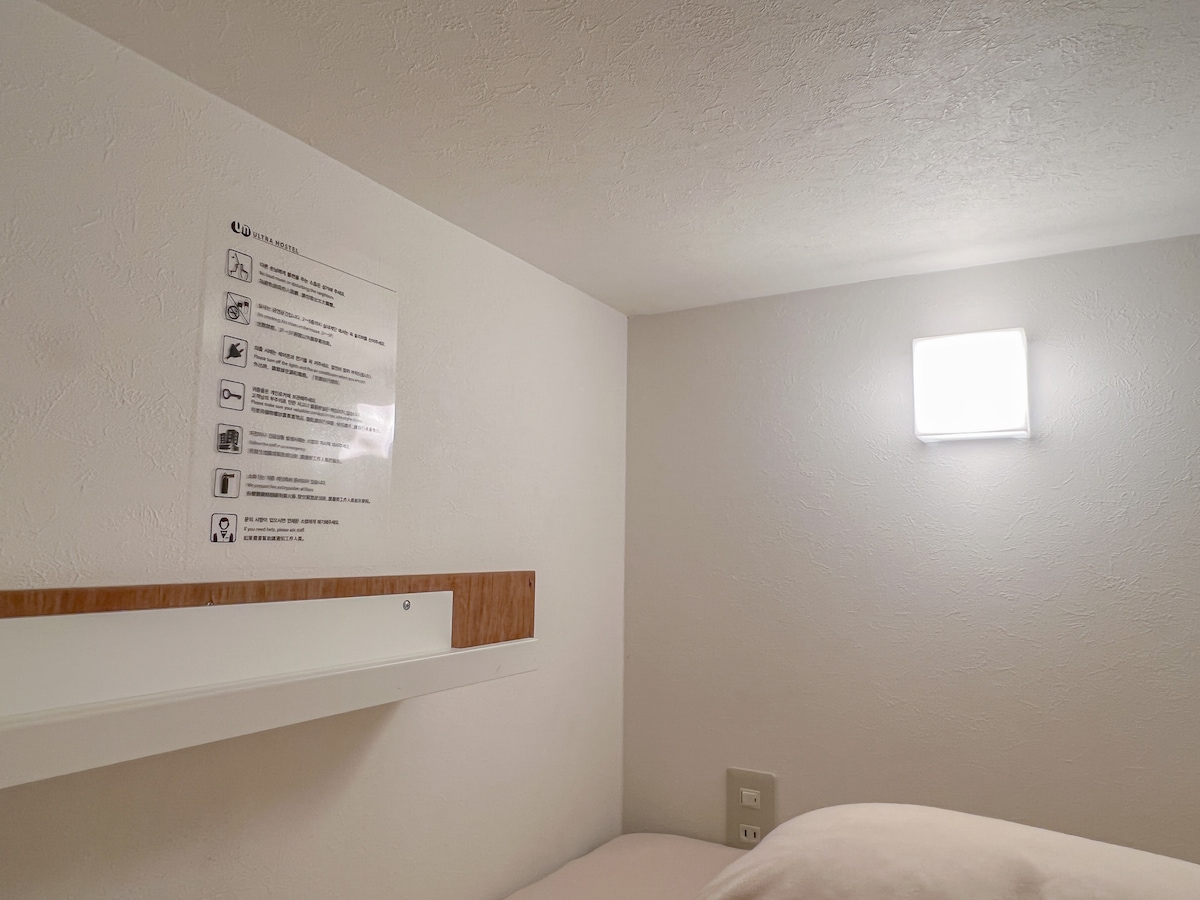 A cozy private capsule features a shelf for personal items and a soft light source mounted on the wall. Details provide essential information for guests, ensuring a practical and user-friendly environment.