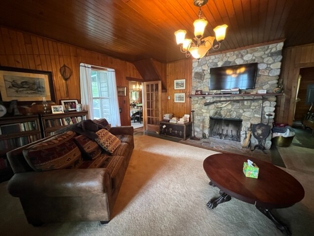 A spacious living room is defined by warm wooden paneling and a stone fireplace. A large brown sofa is positioned near a round table, while a television hangs above the fireplace. Light enters through a set of double doors, enhancing the cozy ambiance.