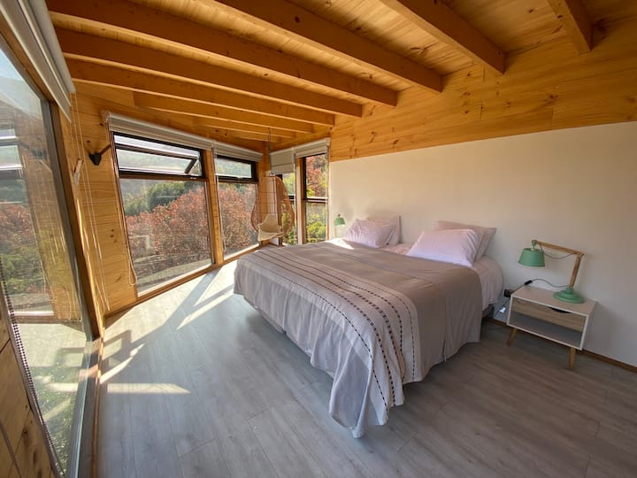 Izba Viento, manželská posteľ SUPER King, čierne záclony a záclony na všetkých oknách, prútené hojdacie kreslo s výhľadom na kopce.