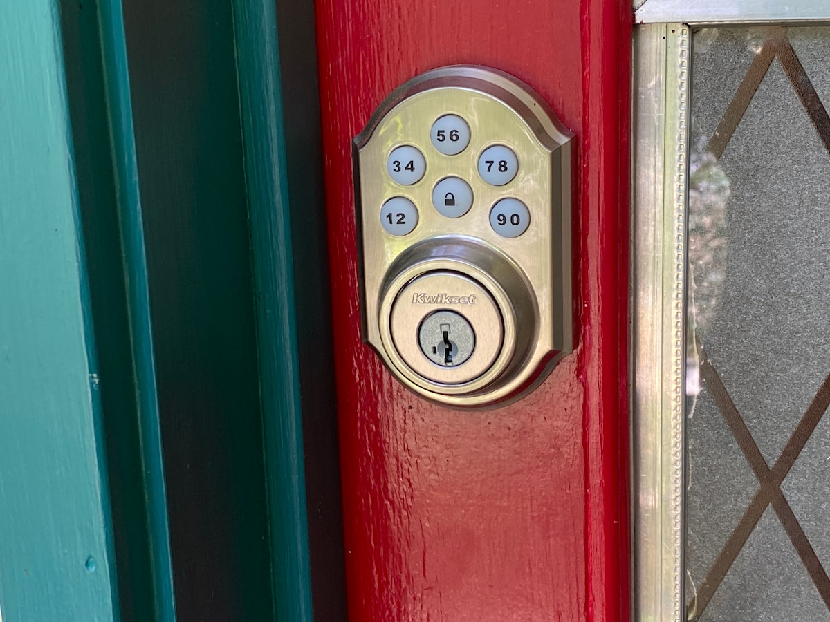 A keyless entry system is shown, featuring a numerical keypad and a traditional keyhole. The vibrant red door frame contrasts with the metallic finish of the lock, providing a convenient and secure check-in option for guests.
