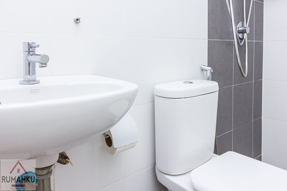 The bathroom features a modern sink with a sleek faucet positioned above a white countertop. A white toilet complements the setup. The shower area is fitted with a wall-mounted showerhead, and the space is accented by neutral tiles in light and dark shades.