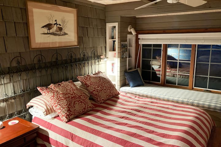 Queen size bed with Pottery Barn linens is in a cozy hideaway room bordered by the front porch and dining area. The large window seat is perfect for reading, a catnap, or to enjoy the sweeping views of the Chesapeake Bay.