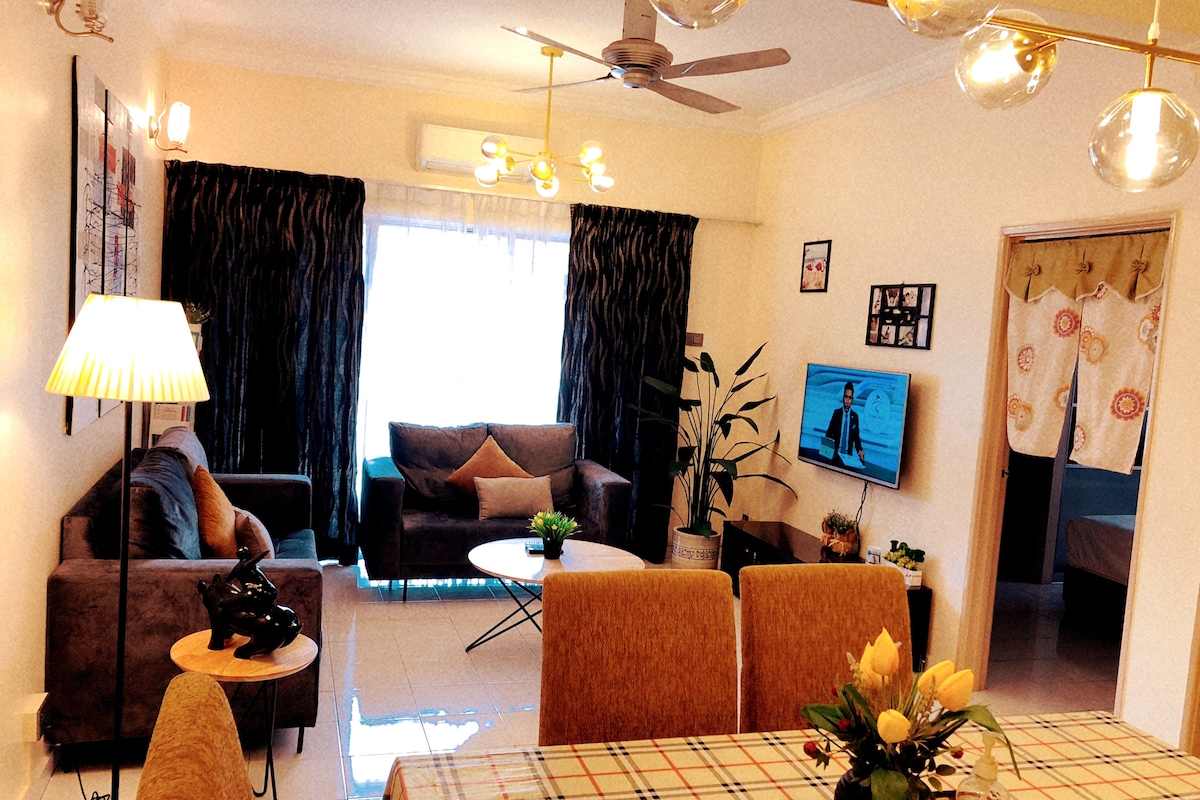 The living area features a comfortable seating arrangement, including a plush sofa and armchair, with a coffee table resting on a tiled floor. A wall-mounted TV displays a vibrant image. Soft lighting is provided by stylish fixtures, and large windows allow natural light to fill the space.