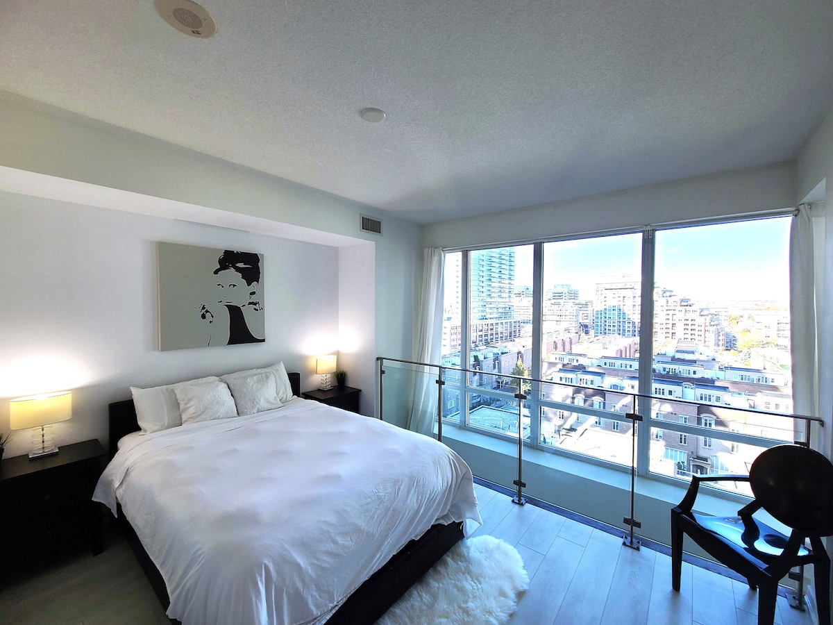 ห้องนอนแบบเปิดโล่งเตียงควีนไซส์ตู้เสื้อผ้าประตูบานเลื่อนคู่เครื่องซักผ้าเครื่องอบผ้าห้องน้ำในตัวโต๊ะข้างเตียงหน้าต่างบานใหญ่พร้อมผ้าคลุมหน้าต่างพื้นที่ลอฟท์เปิดโล่งไปยังชั้นหลัก 