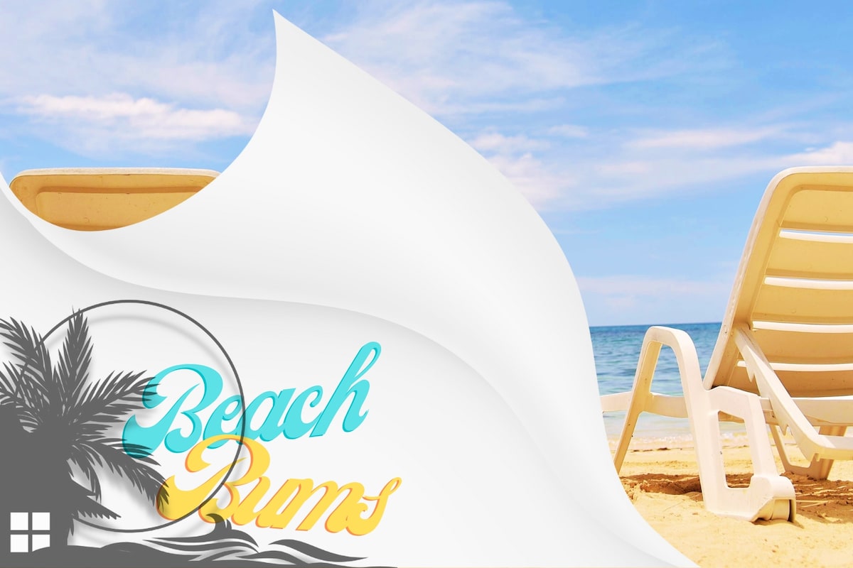 Two lounge chairs are positioned on a sandy beach, facing a calm ocean under a clear blue sky. The inviting scene is accented by gentle waves lapping at the shore, suggesting a serene atmosphere for relaxation.