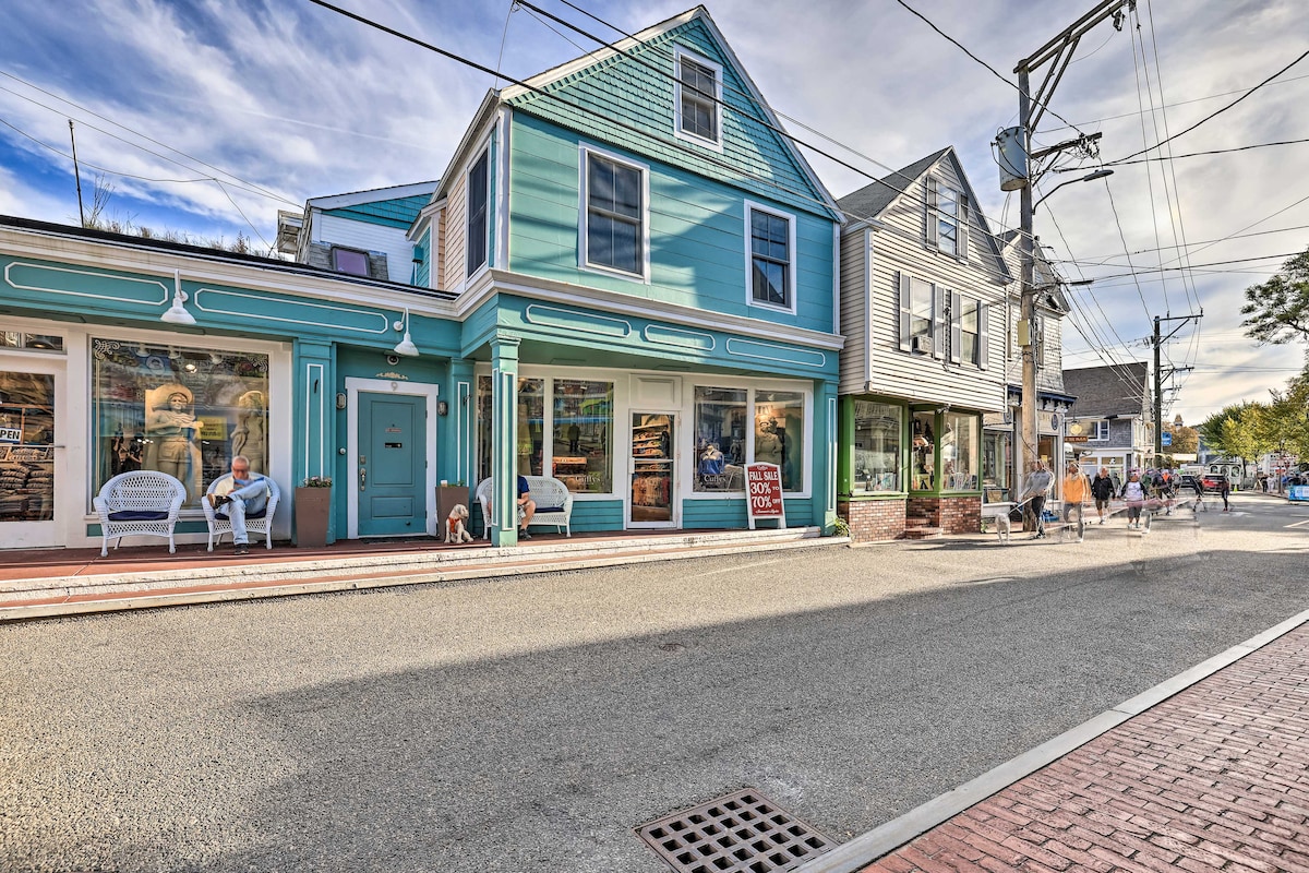 A charming multi-colored building is featured on a lively street, with large display windows showcasing retail spaces. The street is lined with sidewalks, and pedestrians can be seen enjoying the area. The sky above is bright with soft clouds.