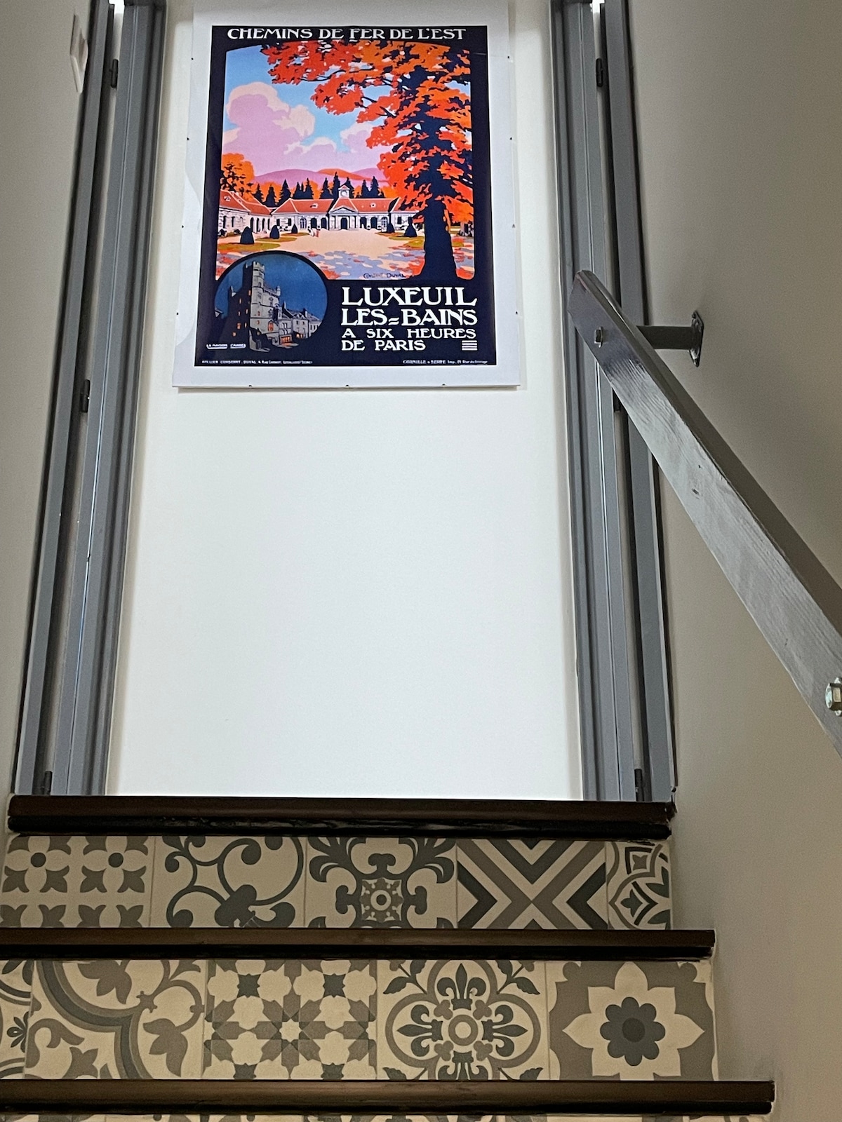 A staircase is featured, leading to the upper level. Decorative tiles adorn the steps, providing visual interest. A vintage travel poster is displayed on the wall, adding character to the space. The open railing allows natural light to illuminate the area.