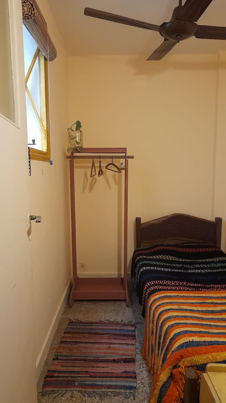 Bedroom. Single bed. With a clothing rack, shelves, and dresser (at the foot of the bed). 
The window overlooks one lung of the building.