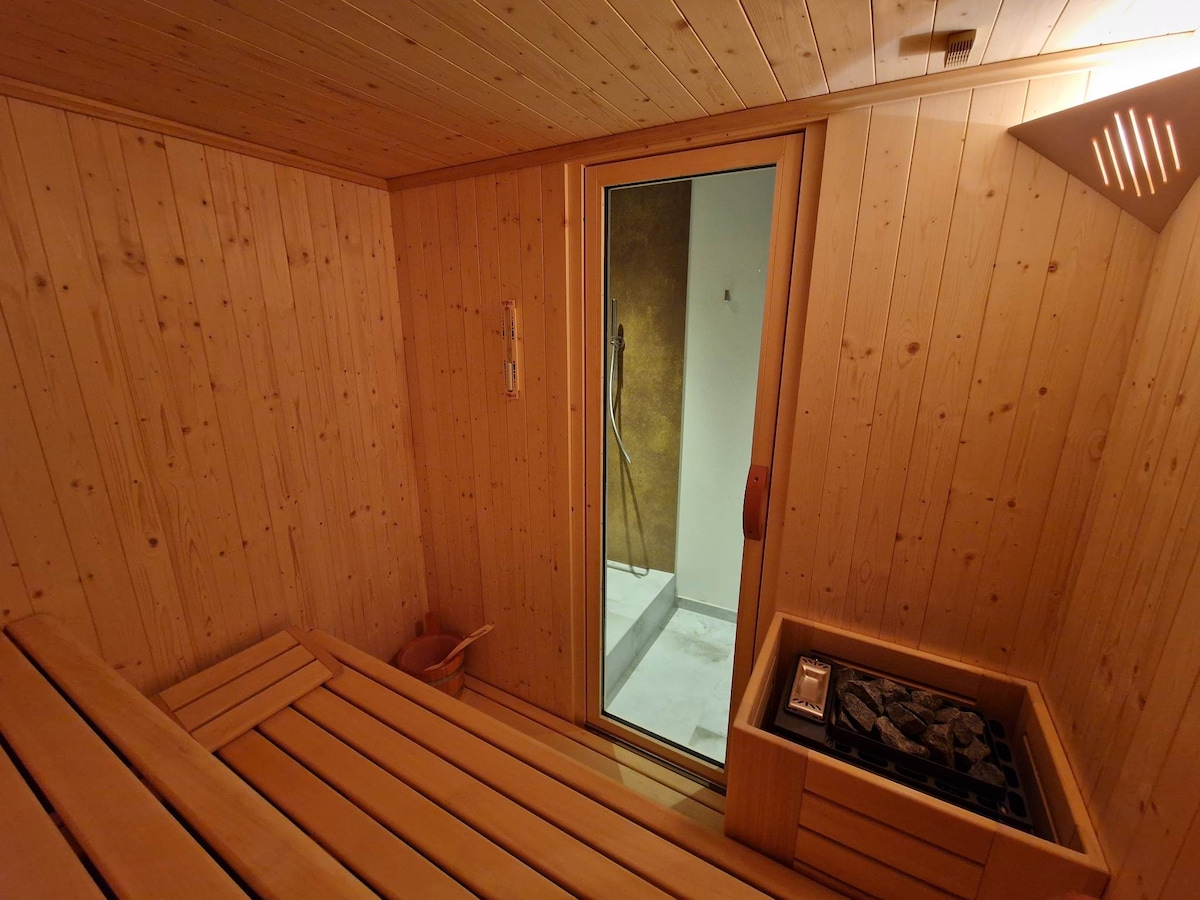 A wooden sauna room is depicted, featuring horizontal wooden benches that promote relaxation. A glass door provides entrance to the sauna, leading to a cool-down area visible in the background. The room is illuminated with soft overhead lights, enhancing the serene environment.