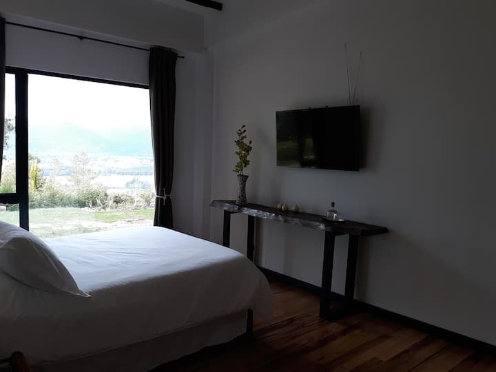 Hermosa vista desde una cama tamaño queen con 2 mesitas de noche y sus lámparas