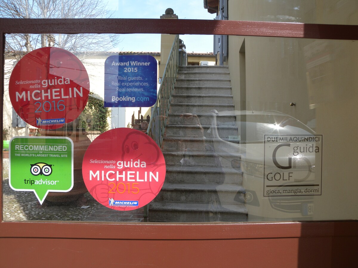 A window display features various accolades, including Michelin awards from 2015 and 2016, along with a TripAdvisor recommendation. Reflections of stairs and surroundings are visible through the glass, emphasizing the inviting entrance of the building.