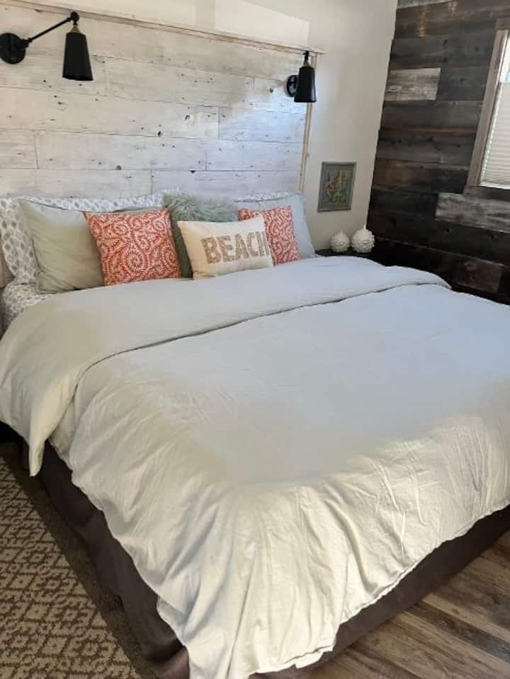 سرير كينج مريح مع إضاءة فوق الرأس ، وستائر معتِّمة أيضًا.  ومروحة سقف.