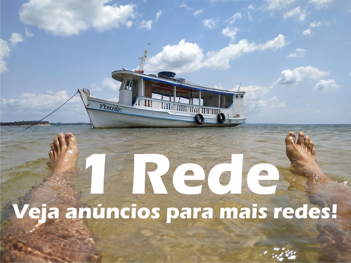 A serene view of the boat, named Vencedor, anchored in shallow waters under a clear sky. The image captures a pair of feet relaxing in the water, inviting a sense of leisure and tranquility by the river.