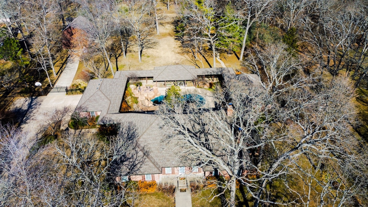 An aerial view showcases the expansive layout of the property, highlighting the guesthouse connected to the main house by a breezeway. The inviting pool area is centrally located, surrounded by a spacious yard and mature trees, offering ample outdoor space for relaxation.