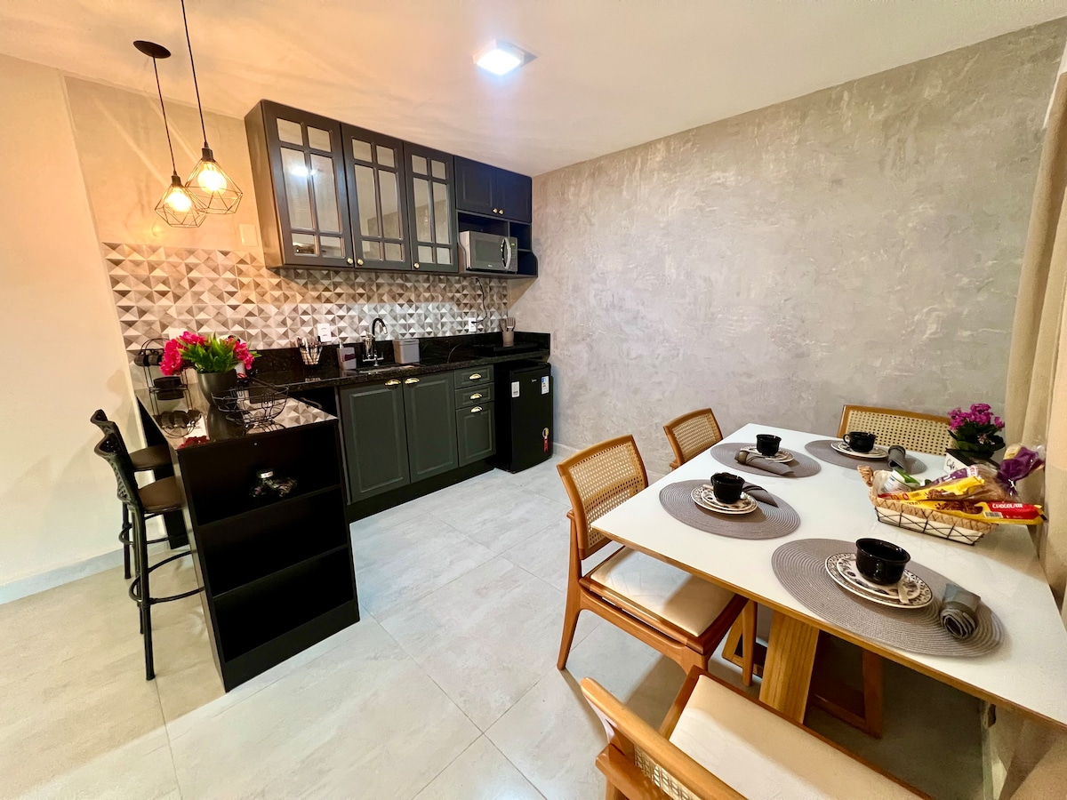 A modern kitchen and dining area features sleek cabinetry and a textured backsplash. A dining table is set with place settings for four, while bar stools are positioned at a kitchen counter. Soft lighting enhances the inviting atmosphere.
