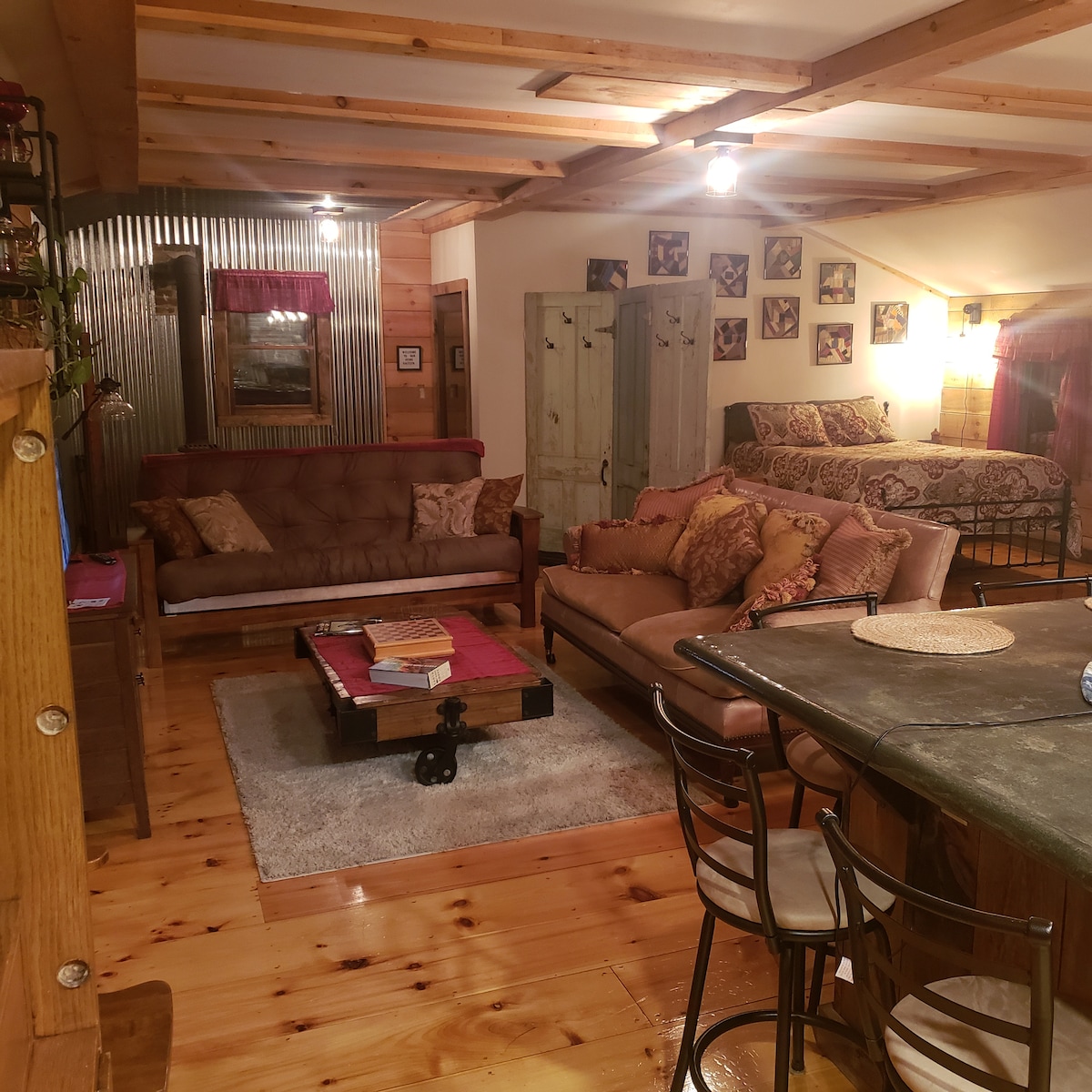 A cozy living area features a mixture of seating options, including a tufted sofa and a vintage-style sofa adorned with decorative cushions. Natural wood floors enhance the warmth of the space, while artwork on the walls and a circular coffee table complete the inviting atmosphere.