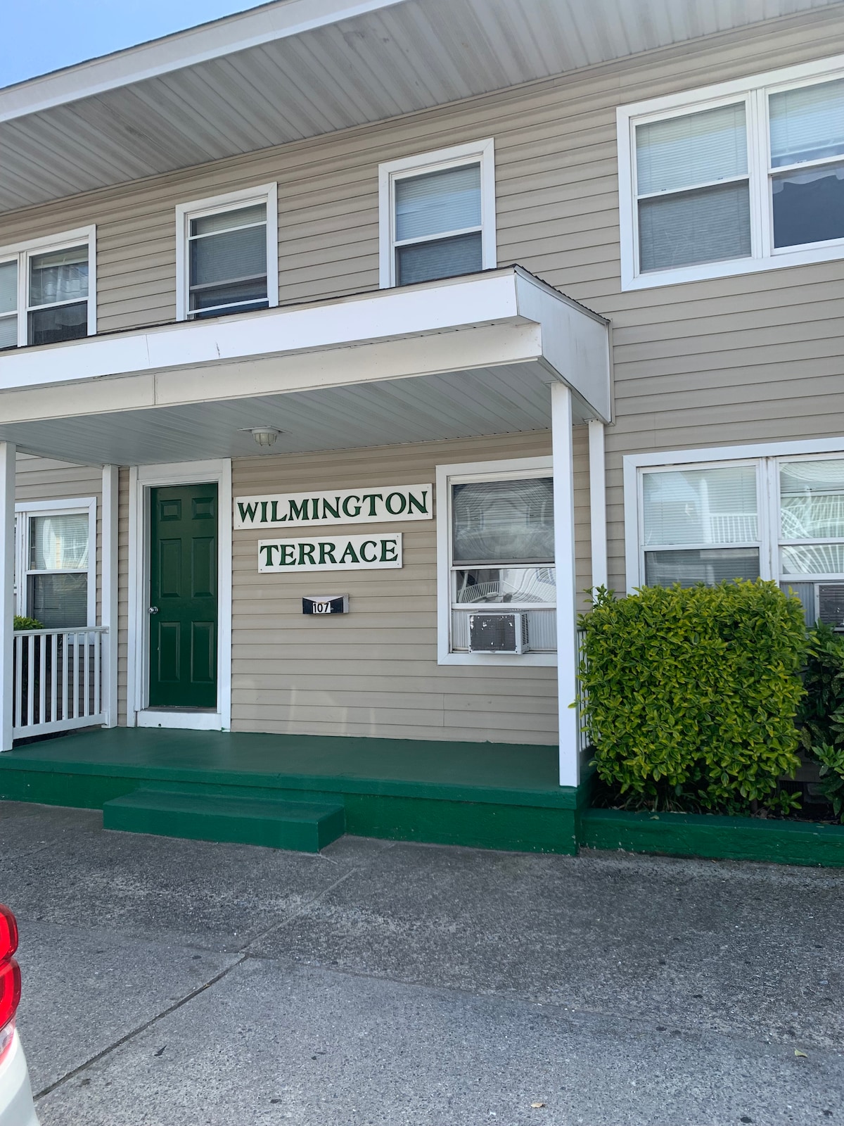 The exterior of the building, featuring a welcoming green door, is complemented by a sign reading 'Wilmington Terrace.' Large windows allow natural light to fill the space, while well-maintained greenery enhances the curb appeal.