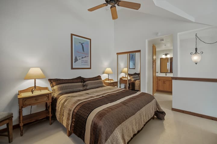 Quarto com cama king size, banheiro anexo, ventilador de teto para maior conforto e armazenamento em armário espelhado, criando um retiro aconchegante e funcional.