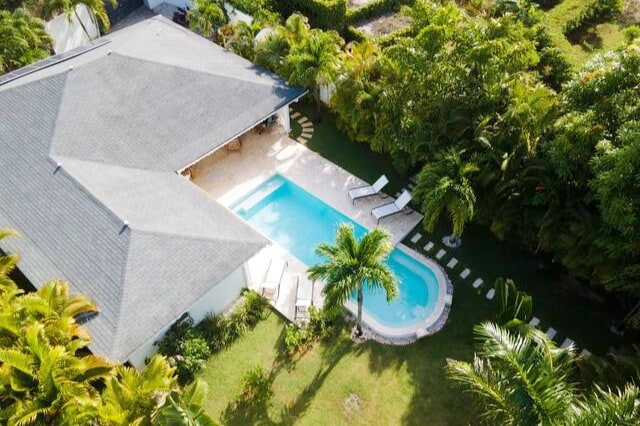 An aerial view of a tropical villa surrounded by lush greenery, featuring a private infinity pool with sun loungers nearby. The landscaped garden is dotted with palm trees, showcasing a vibrant and tranquil outdoor space.