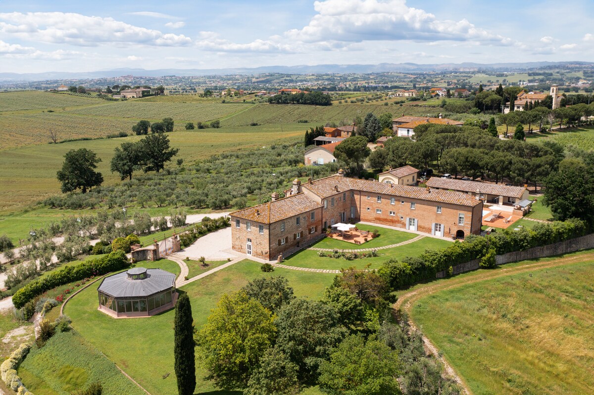 Aerial view of a beautifully restored farmhouse surrounded by lush green hills and vineyards. The spacious property features manicured gardens and outdoor seating areas. Scenic countryside landscapes stretch into the distance, providing a sense of tranquility and natural beauty.