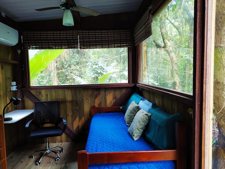 غرفة معيشة مع مكيف هواء ومروحة سقف وتلفزيون ذكي ومساحة للمكاتب المنزلية وسرير أريكة.