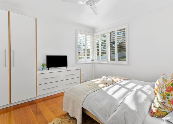 ห้องนอนพร้อมเตียงควีนไซส์พัดลมเพดานและทีวี