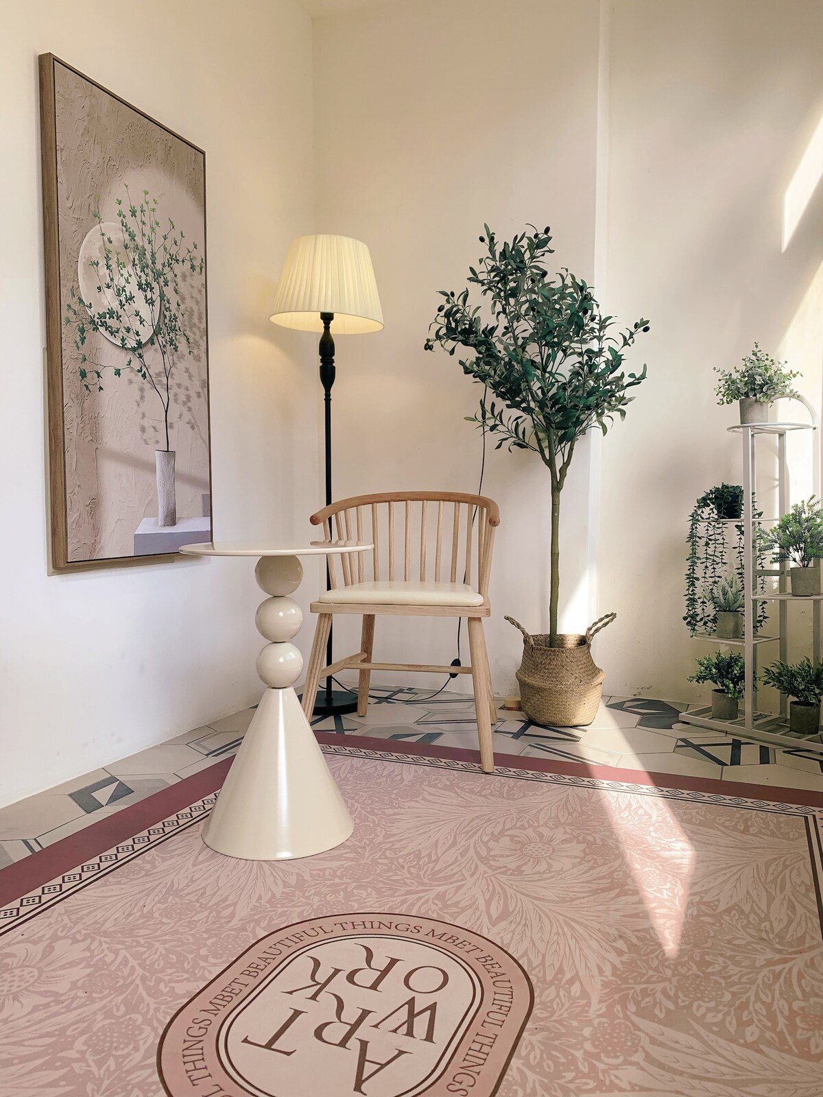 A light-filled corner features a modern chair beside a round table. A decorative plant stands next to the chair, while potted greenery adds a natural touch. A wall art piece with a botanical theme complements the inviting ambiance, highlighted by a soft floor rug.