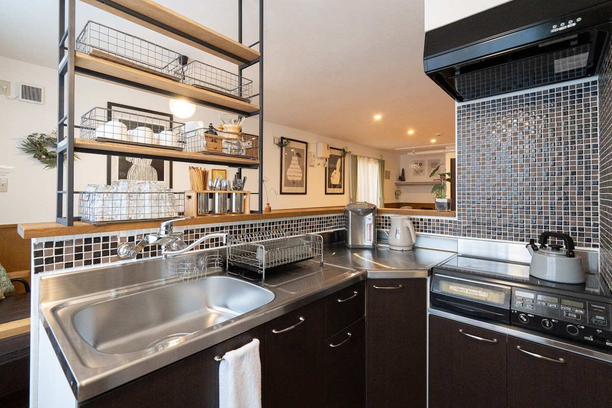 A functional kitchen is showcased, featuring stainless steel appliances and a spacious sink. Open shelving displays organizers and kitchenware, while a mosaic backsplash adds texture. The countertop is equipped with a kettle and other essentials, ensuring convenience for meal preparation.