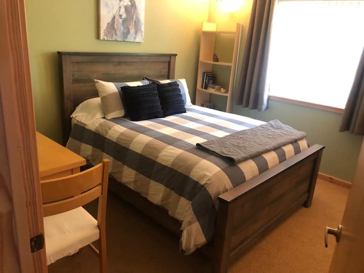 Segundo dormitorio con cama tamaño queen, colchón y ropa de cama nuevos y un pequeño escritorio/área de trabajo con lámpara.