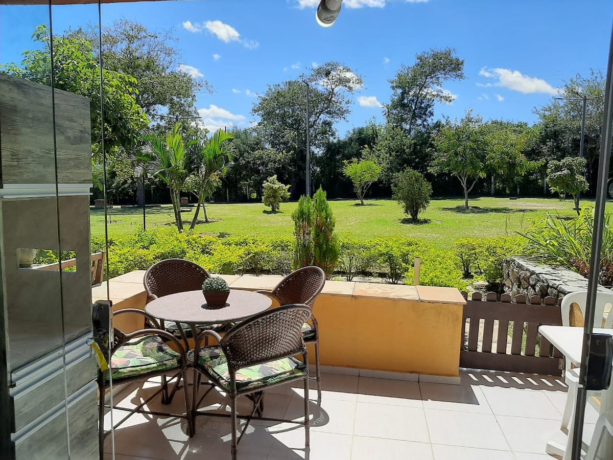 A spacious outdoor terrace features a circular table surrounded by four wicker chairs. Lush greenery is visible in the garden area, providing a serene view of the landscape beyond.