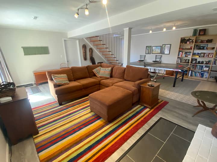 غرفة في الطابق السفلي بها أريكة وتلفزيون وطاولة تنس الطاولة.  يفتح على الفناء الخلفي. 