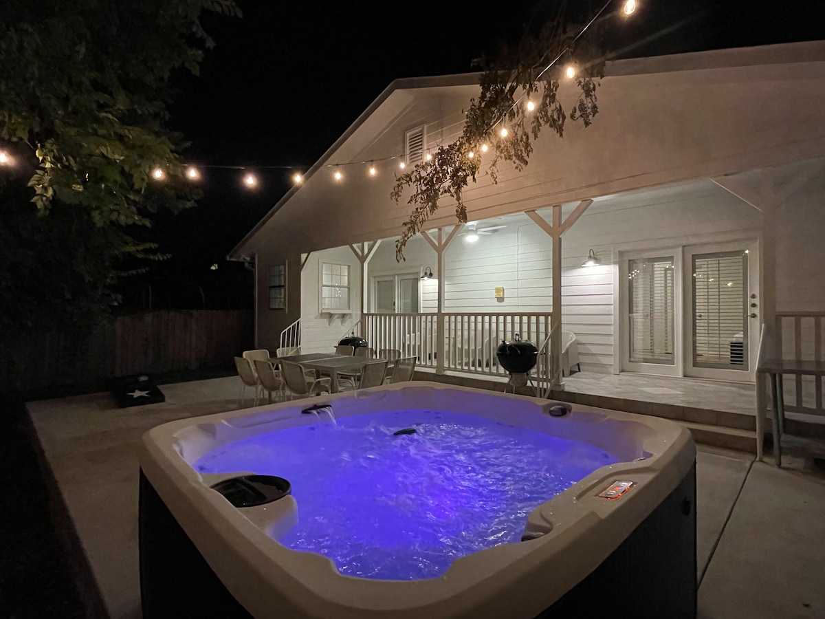 A therapeutic hot tub is illuminated with soft blue lighting in the foreground. In the background, a private patio area with seating can be seen, under warm string lights, creating an inviting outdoor space.