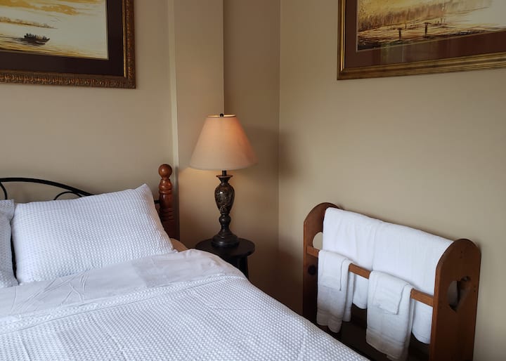 Ground floor bedroom has a queen bed, blackout curtains and is adjacent to a full bathroom with shower. Original local art graces the walls. This room is ideal for those who prefer to avoid the stairs.