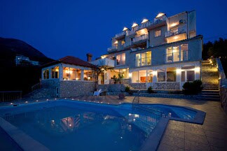 An expansive villa is illuminated at night, featuring multiple levels and balconies. A swimming pool reflects the lights from the surrounding structures. The outdoor area includes a covered patio, enhancing the space for relaxation and entertainment.