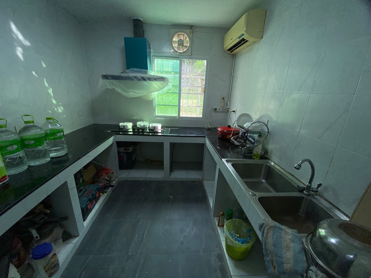 The kitchen features a practical layout with a black countertop and dual sinks. Modern appliances are neatly arranged, including a stove beneath a ventilation hood. Natural light enters through a window, illuminating the work surfaces. Storage areas are organized to enhance functionality.