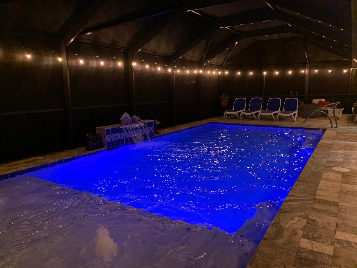 A heated saltwater pool is illuminated with blue lighting, creating a serene atmosphere in the screened-in lanai. Surrounding the pool are several lounge chairs, inviting relaxation. Soft lighting above casts a gentle glow throughout the space, enhancing evening enjoyment.